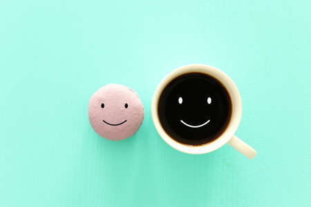 cup of coffee and colorful macaroon with happy face on wooden mint backgroundの写真素材