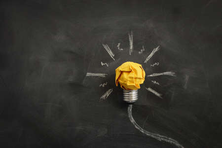 Education concept image. Creative idea and innovation. Crumpled paper as light bulb metaphor over blackboardの写真素材