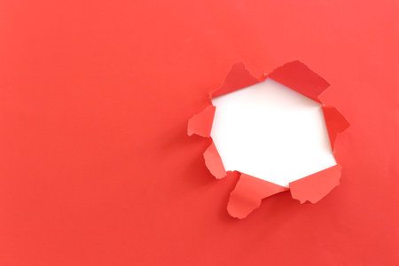 Close up of hole torn in red paper background.の写真素材