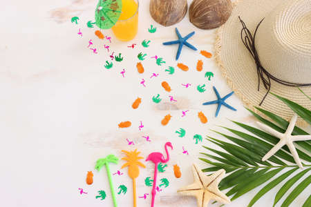 nautical concept with palm leaf, beach hat, frui cocktail and starfish over white wooden background