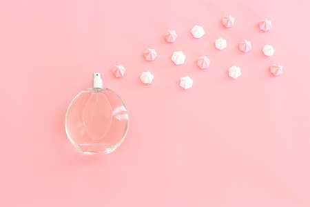 Top view of perfume bottle with meringue over pastel pink background. Cosmetics, fragrance and...