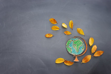 Back to school concept. Top view banner of globe with autumn dry leaves over classroom blackboard backgroundの写真素材