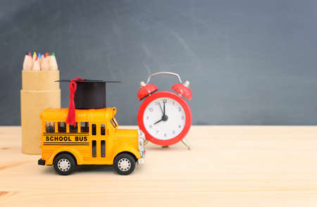 education and back to school concept. yellow bus with graduation hat over wooden desk