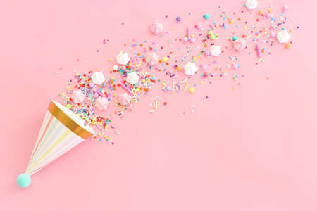 Birthday party background with hats and colorful candies over pastel pink background. Top viewの写真素材