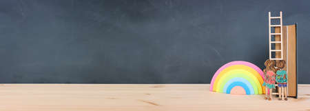 Back to school concept. Top view image of two kids standing next to ladder and book over wooden deskの写真素材