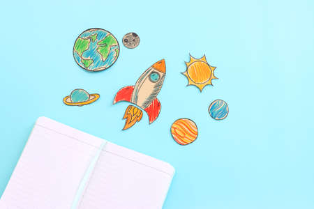 Painted rocket, planets and open blank notebook over blue background