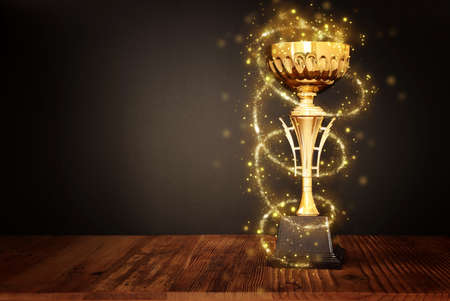 low key image of gold trophy over wooden table and dark background, with abstract shiny lightsの写真素材