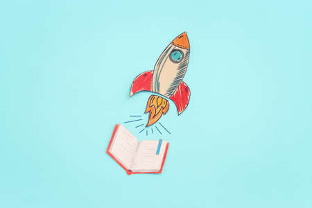 Painted rocket and open notebook over pastel blue background