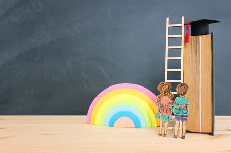Back to school concept. Top view image of two kids standing next to ladder and book over wooden deskの写真素材