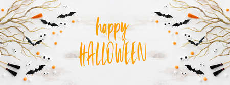 top view image of Halloween holoday. witcher broom, bare trees, treats and bats over white wooden tableの写真素材