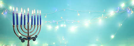 Image of jewish holiday Hanukkah with menorah (traditional candelabra) and candles over garland glitter lights backgroundの写真素材