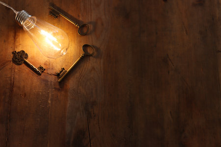 vintage key under bright lightbulb over wooden table. concept of finding the best solution