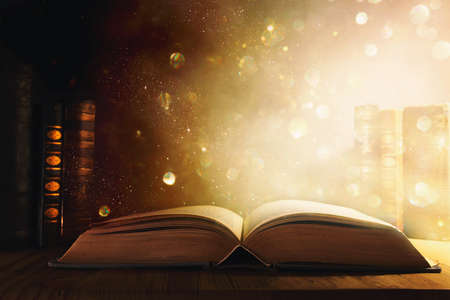 image of open antique book on wooden table with glitter overlay