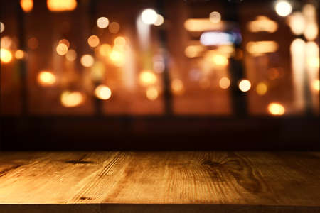 background Image of wooden table in front of abstract blurred restaurant lightsの写真素材