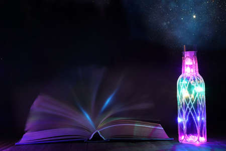 image of mystic bottle with glitter lights next to antique book on wooden table