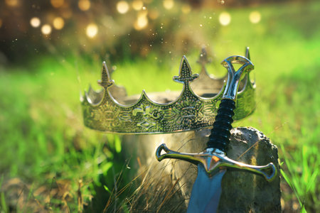 mysterious and magical photo of gold king crown and sword over stone in the England woods. Medieval...