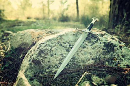 mysterious and magical photo of silver sword in the England woods over stone. Medieval period conceptの写真素材