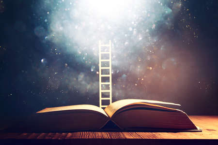 image of open antique book on wooden table with glitter overlayの写真素材