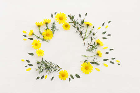 Top view image of yellow chrysanthemum field flowers composition over wooden white background. Flat...