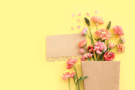 Top view image of pink flowers composition and empty note over yellow pastel background