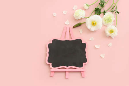 Top view image of white flowers composition and empty blackboard over pink pastel backgroundの写真素材