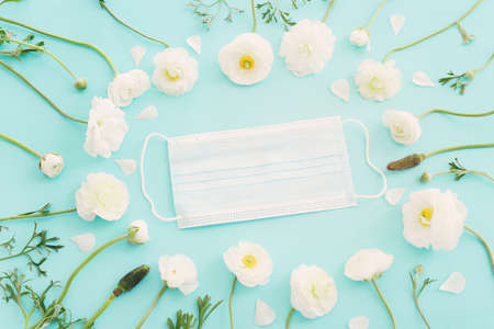 Protective surgical face mask and flowers over wooden blue background. Spring allergy concept. Flat lay, top view.の写真素材