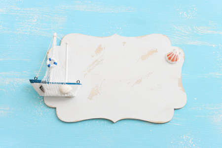 nautical concept with white sail boat, seashell and blank board for copy space over blue wooden backgroundの写真素材