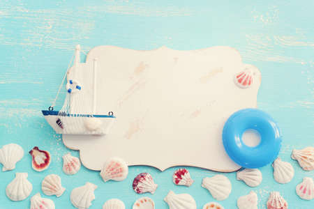 nautical concept with white sail boat, seashells and blank board for copy space over blue wooden...