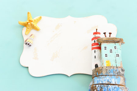 nautical concept with house and lighthouse driftwood, seashells, star fish, blank board for copy space over mint blue wooden backgroundの写真素材