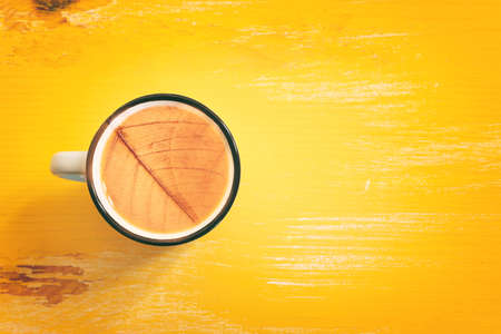 Top view image of coffee cup over wooden yellow table and autumn leaves metaphor