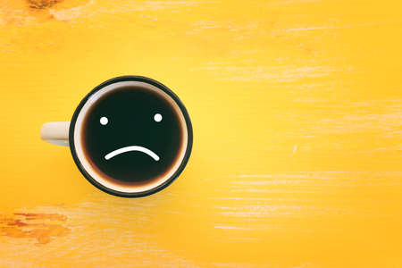 Top view image of coffee cup and sad face. Metaphor for sadness or unhappy emotionsの写真素材