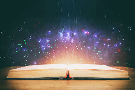 image of open antique book on wooden table with glitter overlay