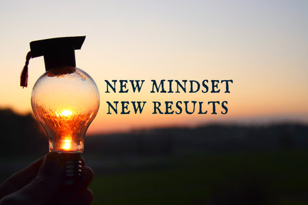 Hand holding light bulb with the text new mindset in front of the bright sunの写真素材