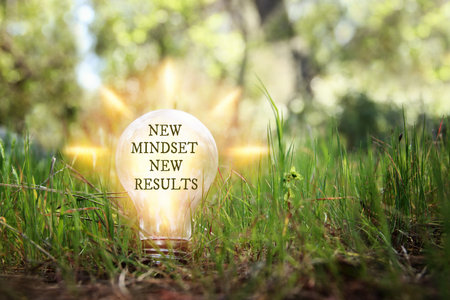Hand holding light bulb with the text new mindset on the green grassの写真素材