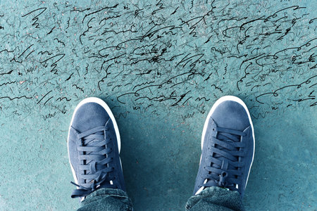 Top view image of person with sneakers on asphalt with cracks. Concept of confusion and doubtの写真素材