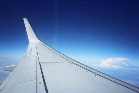 View of wing of an airplane through the window, against a blue sky and clouds