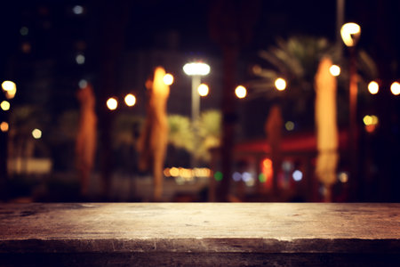 image of wooden table in front of abstract blurred background of restaurant lightsの写真素材