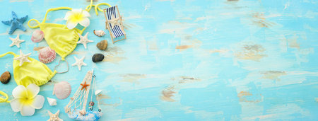 Top view of female swimsuit bikini, starfish, boat and monoi flower over wooden pastel blue...