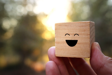 Hand holding wooden cube with smiling face at sunset time. Concept of happiness and satisfactionの写真素材