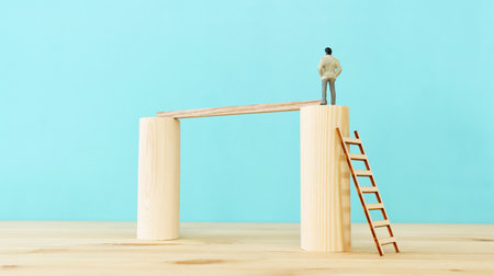 business concept picture of challenge. A man figure stands on the edge of high wall and passes the gap by placing a ladder or bridge. Problem solving ideaの写真素材
