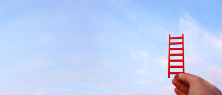 Hand holding red ladder in front of sky. Concept of aiming high and achieving successの写真素材