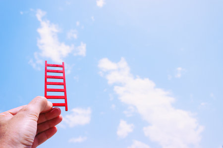 Hand holding red ladder in front of sky. Concept of aiming high and achieving successの写真素材