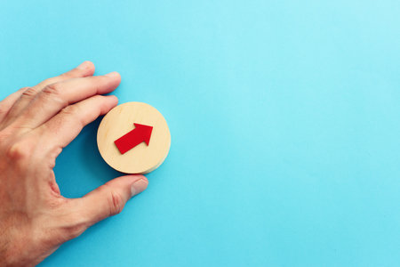 Hand holding cube with red arrow on textured paper backgroundの写真素材