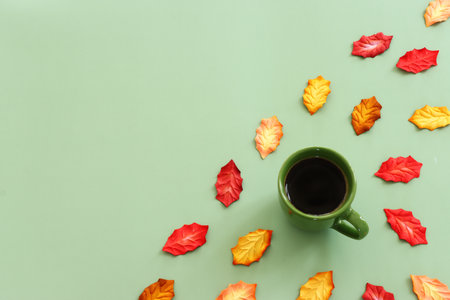 A cup of coffee and autumn leaves on a green pastel background