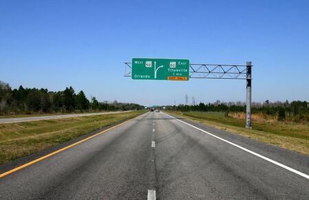 Road fading into Distance with Road sign giving directions in mid-groundの写真素材