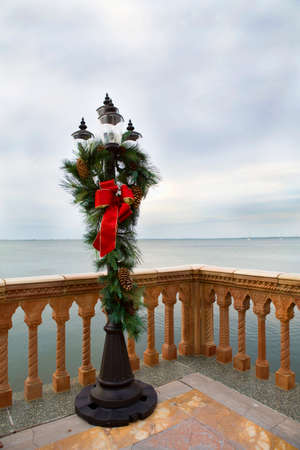 Red Christmas bow, trimmed in gold, hanging from a pine wreath  Pine cones are visible in frame の写真素材