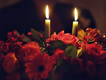 Two candles lighting up an arrangment of flowersの写真素材