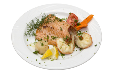 Grilled salmon and shrimps with tomato and lemon on plateの写真素材