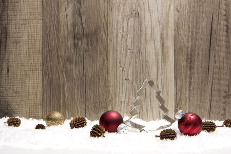 christmas decoration with wooden background, snow, christmas baubles red, gold and pine cones の写真素材