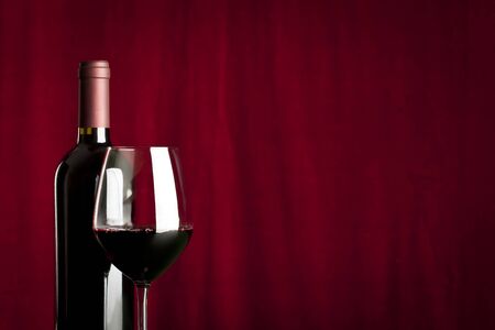 a glass of red wine and a bottle on red backgroundの写真素材